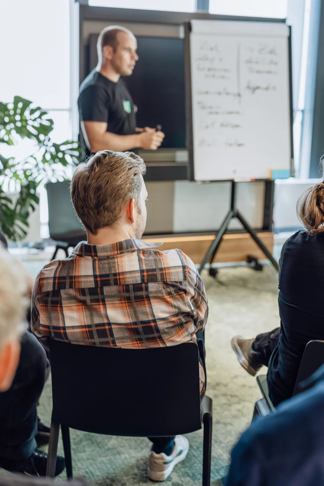 A man presenting to a seated audience using a flipchart in a modern office setting.